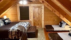 Ein gemütliches Schlafzimmer im Dachgeschoss mit einem Bett, zwei kleineren Betten, einem Deckenventilator und einer Tür.
