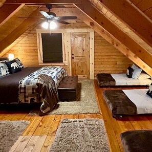 Un dormitorio acogedor en el ático con una cama, dos sofás, un ventilador de techo y una puerta.