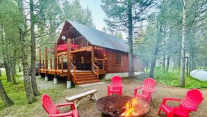 Eine rustikale Holzhütte mit einer Terrasse, einer Feuerstelle und roten Adirondack-Stühlen.