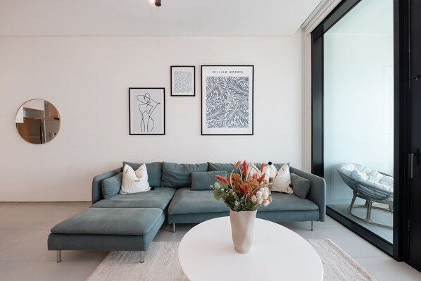 A modern living room with a sectional sofa, a round mirror, and framed artwork on the wall.