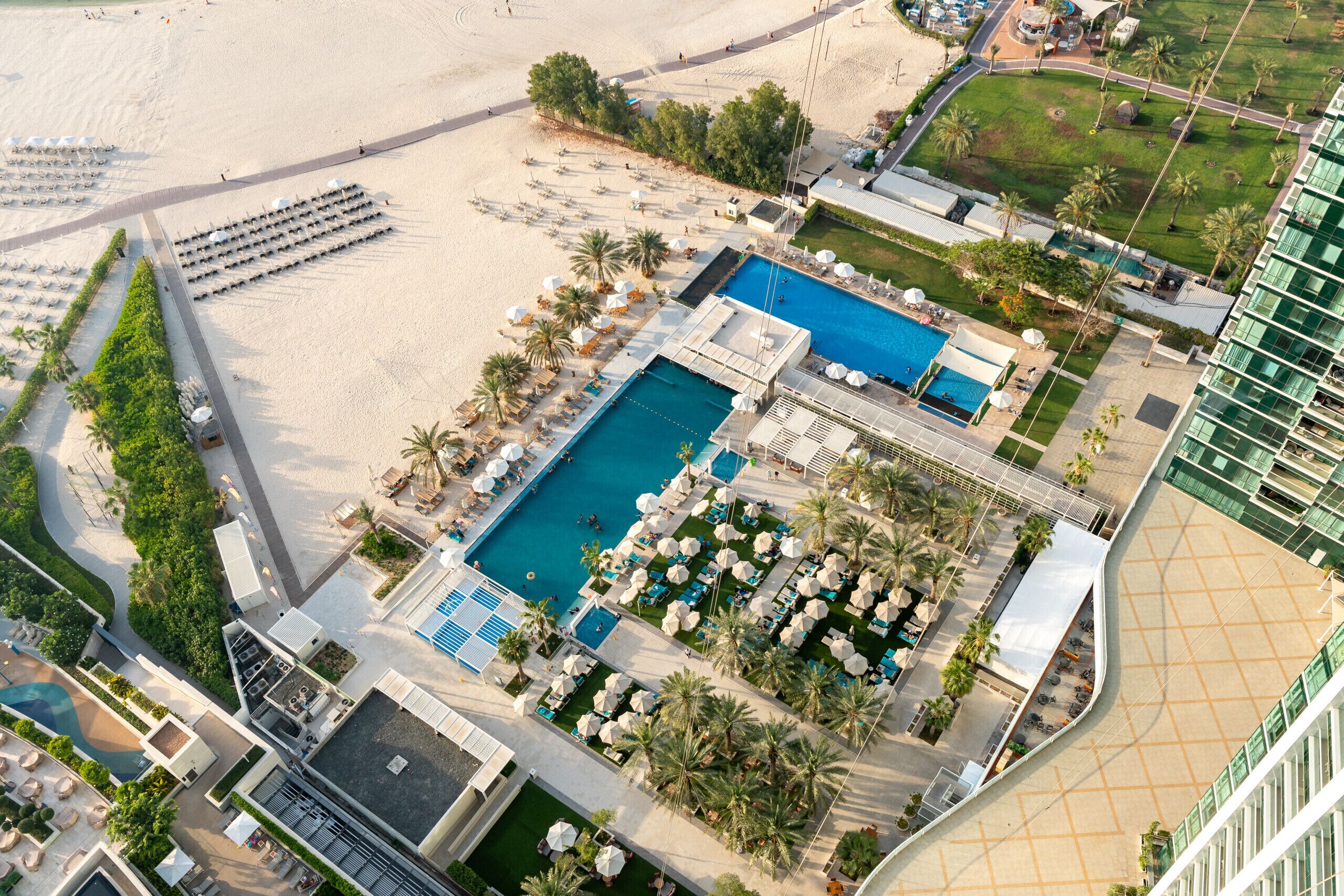 Luchtbeeld van een resort met een centraal gelegen zwembad, ligbedden en palmbomen.