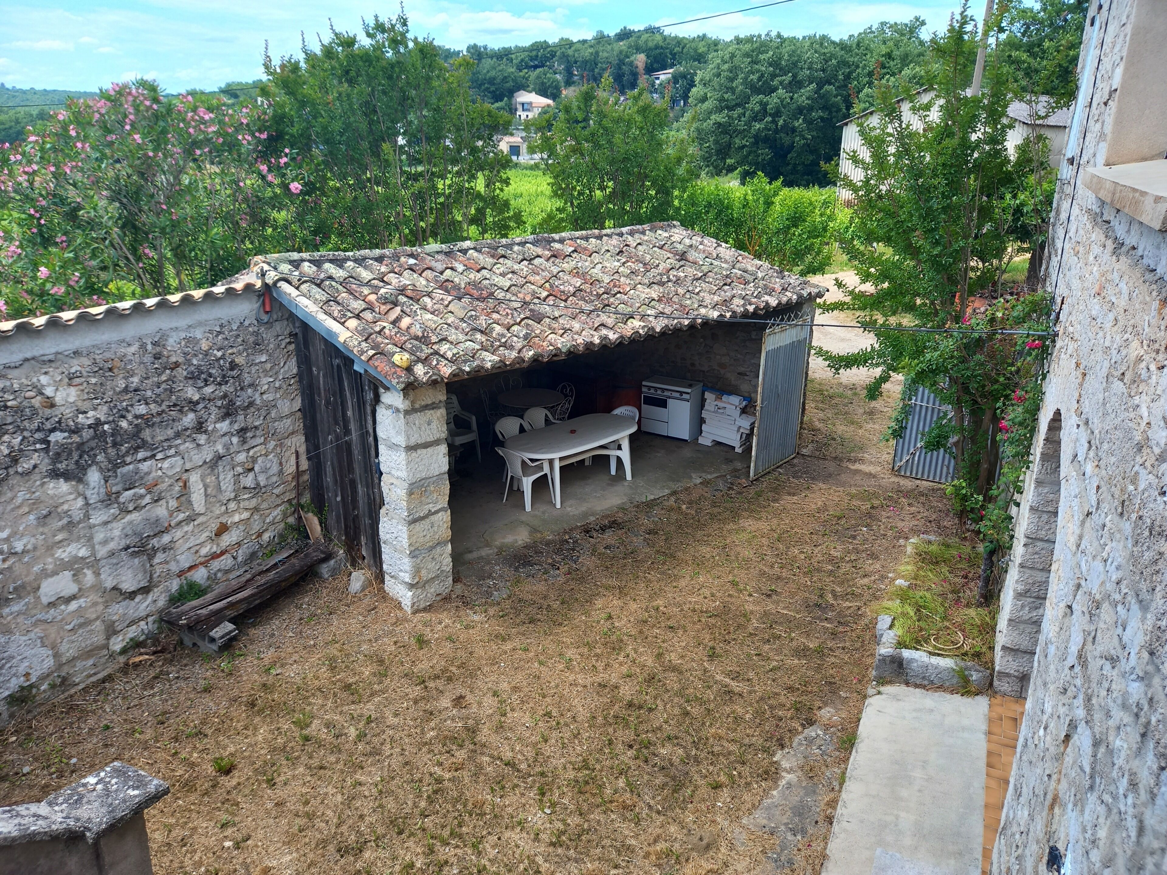 A covered outdoor area with a table and chairs, a stone wall, and a view of a residential area.