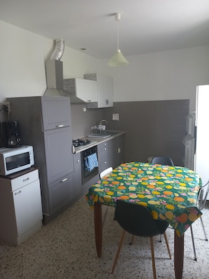 A compact kitchen with a microwave, stove, oven, and a table with a fruit-patterned tablecloth.