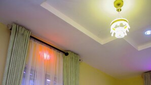 A bedroom with a bed, curtains, a ceiling light, and a nightstand. - BON HOMES (Ibadan)