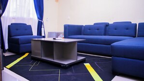 A modern living room with a sectional sofa, a small table, and a window with blue curtains. - BON HOMES (Ibadan)