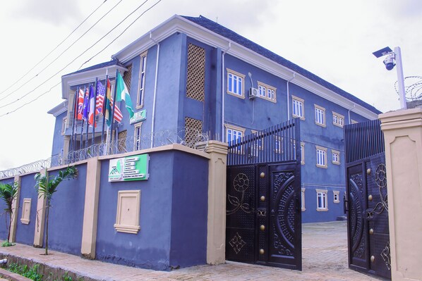 A large, two-story building with a blue facade, a gated entrance, and multiple flags.
