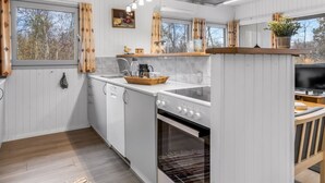 Una cocina moderna con armarios blancos, horno integrado y un amplio ventanal con cortinas.