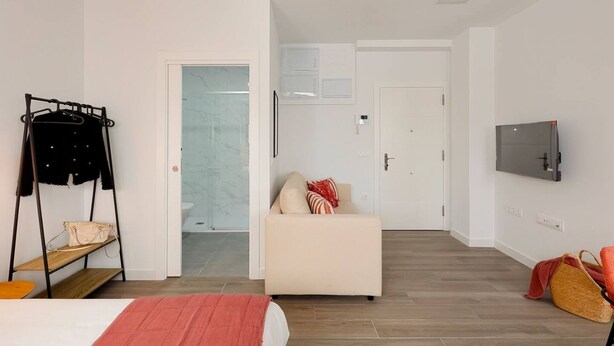 Une chambre d’hôtel comprenant un lit, un canapé, une télévision, un porte-manteau et une porte donnant accès à une salle de bain.