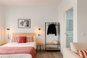 Een slaapkamer met een bed, nachtkastjes, een kapstok, een stoel en een badkamer zichtbaar door een geopende deur.