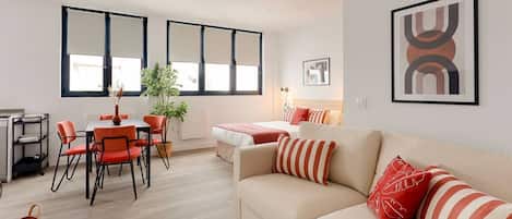Una sala moderna con un sofá, una mesa de comedor con sillas y una cama con una colcha roja.