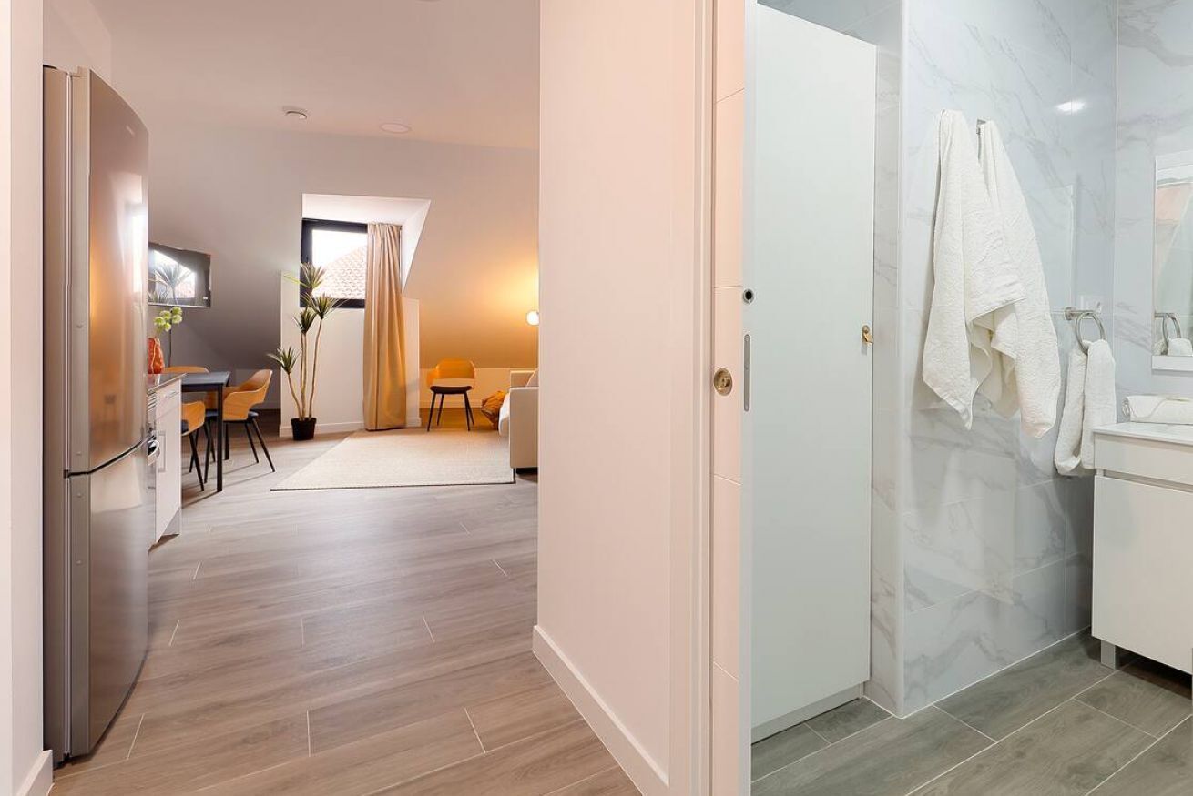 Eine moderne Küche mit Kühlschrank, ein Essbereich mit Stühlen und Tisch sowie ein Badezimmer mit Dusche und Handtuchhalter.