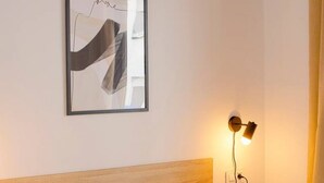 Een slaapkamer met een houten hoofdeinde, een lijstwerk abstract kunstwerk, en een wandlamp.