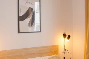 Un dormitorio con cabecera de madera, una obra de arte abstracto enmarcada y una lámpara fijada a la pared.