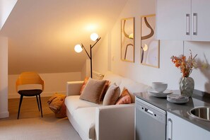 A modern living room with a sofa, a dining table, a chair, and a kitchen area with a dishwasher.