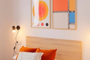 Un dormitorio con cabecera de madera, cama con ropa de cama anaranjada y blanca, y dos obras de arte enmarcadas en la pared.