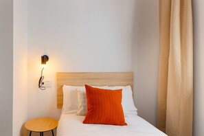 A hotel room with a wooden headboard, a single bed with white and orange pillows, a small round table, and a wall-mounted light fixture. - 644D2 Apartamento 5p Sobrecantu (Oviedo)