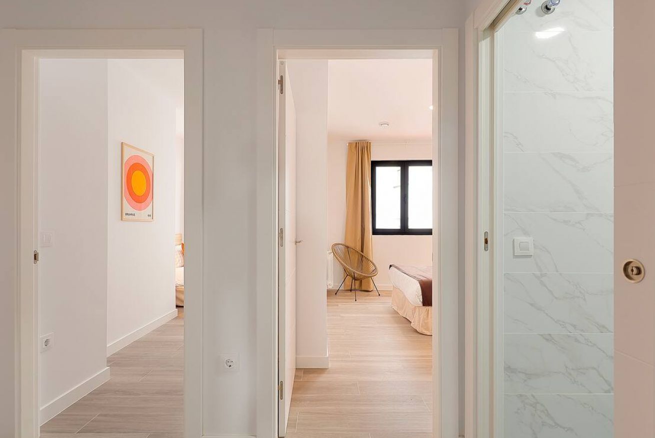 A hallway leading to a bedroom with a bed, a chair, and a window.