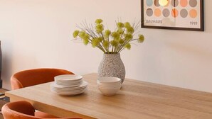 A dining table with a vase of green foliage, a stack of white plates, and a framed artwork on the wall. - 644D2 Apartamento 5p Sobrecantu (Oviedo)
