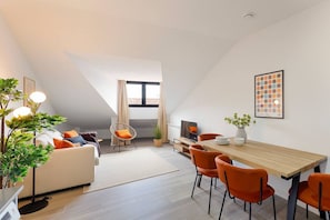 Una sala de estar moderna con un sofá, una mesa de comedor, sillas, un televisor y una planta.