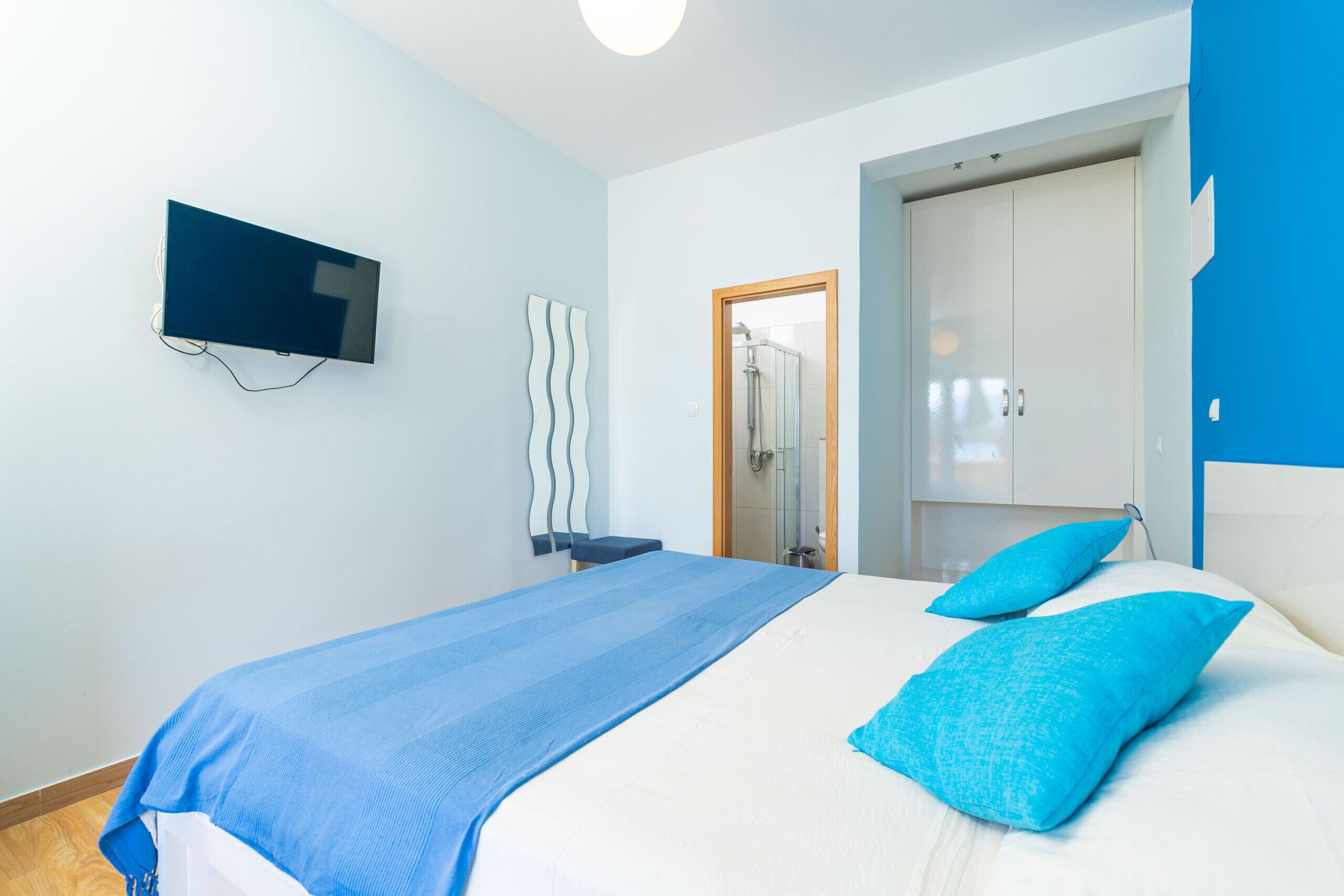 A bedroom with a bed, a television mounted on the wall, a wardrobe, and a door leading to a bathroom.