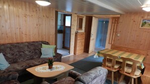 Una habitación acogedora con detalles de madera, un sofá, una pequeña mesa con un mantel de encaje y una zona de comedor con sillas.