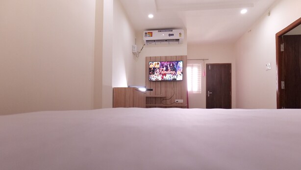 A hotel room with a large bed, a TV mounted on the wall, an air conditioning unit, and a wooden wardrobe. - Hotel Rewa Regency (Huzur)
