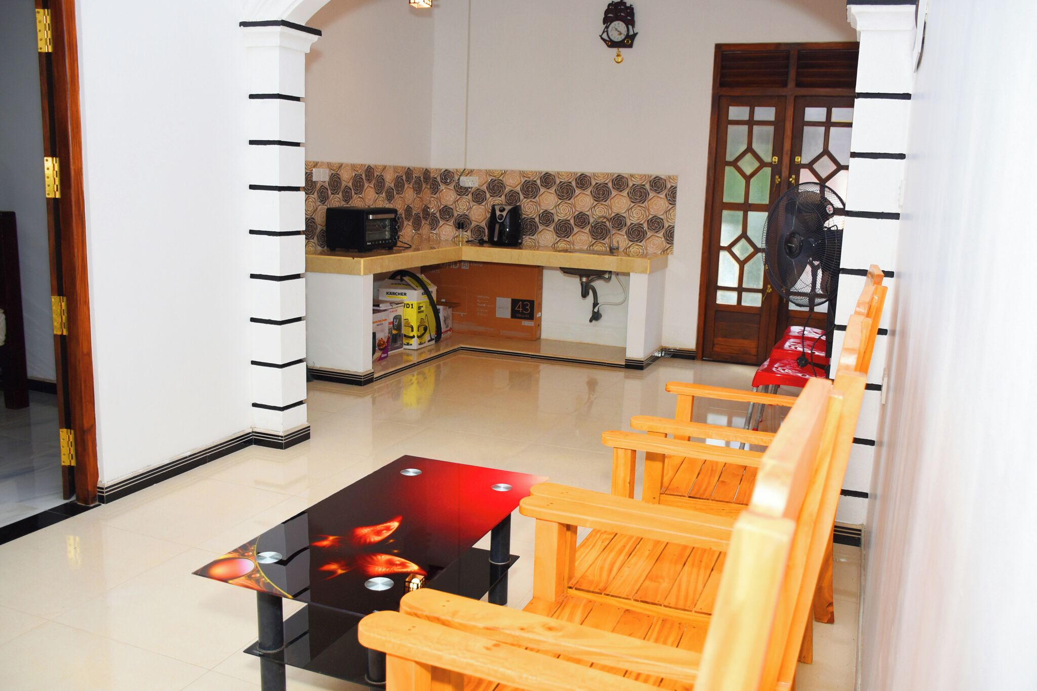 Cocina moderna con microondas, hervidor y cafetera sobre la encimera. En primer plano, una silla de madera y una mesa de vidrio con superficie roja.