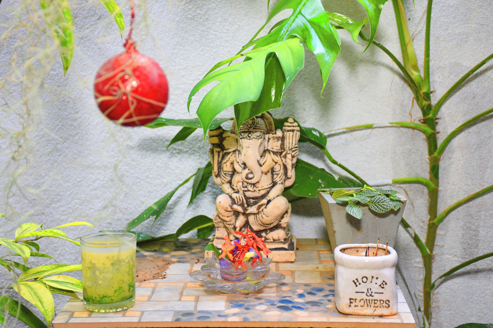 A small altar with a statue, a glass of green liquid, and a pot of flowers.