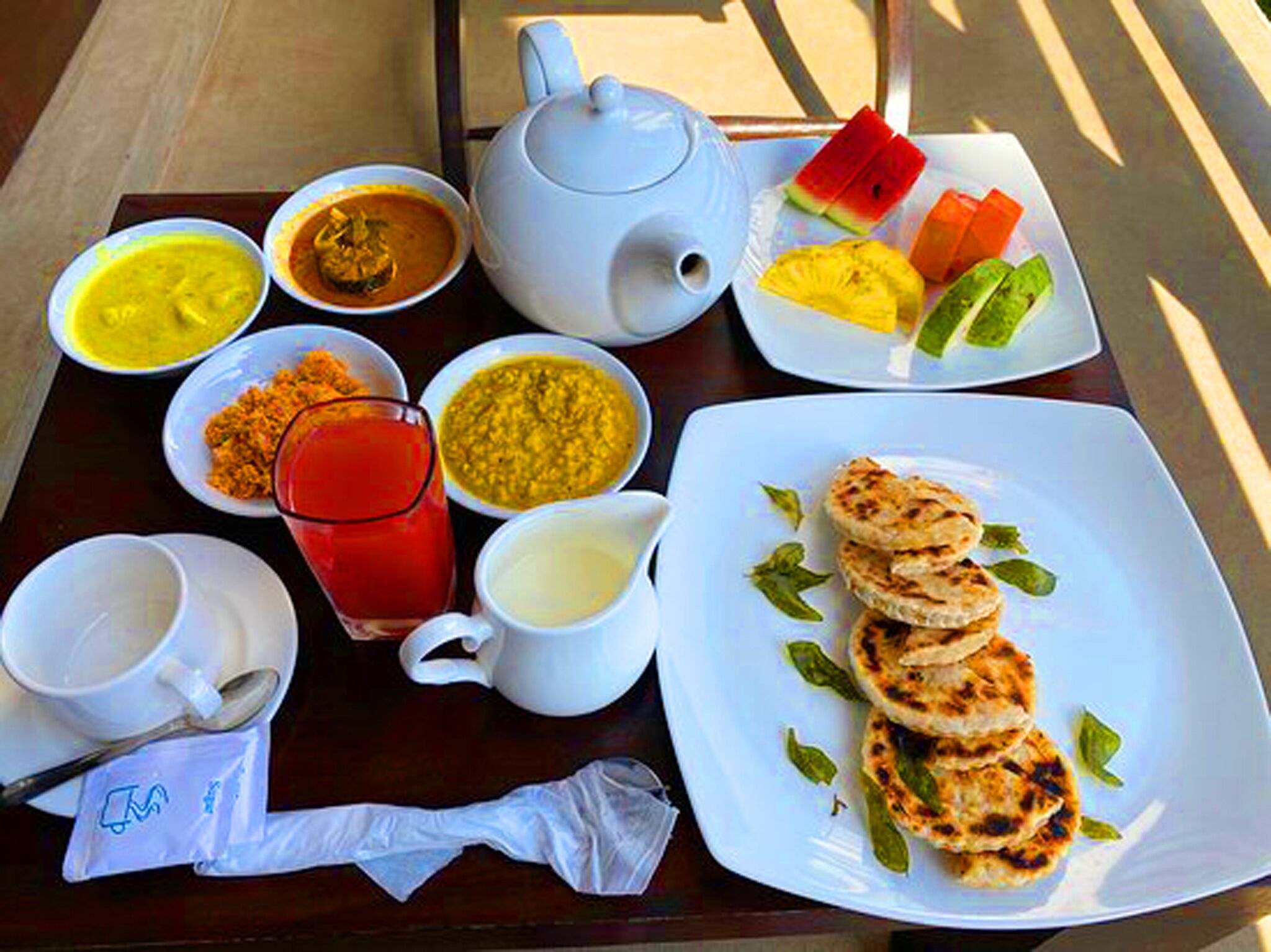 A table with various dishes including a plate of grilled items, bowls of soup, a teapot, and a glass of red drink.