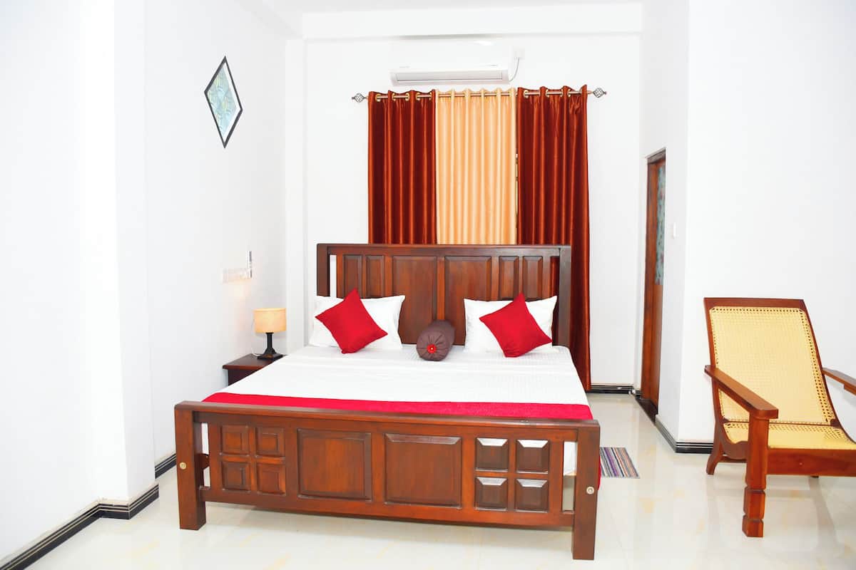 A neatly arranged bedroom with a wooden bed, red pillows, a bedside table with a lamp, and a chair.