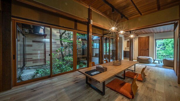 Una habitación amplia con suelo de madera, grandes puertas correderas de vidrio, una mesa de comedor de madera e iluminación colgante moderna.