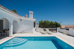 A swimming pool with a tiled deck, a white building with arches, and a clear blue sky. - Villa Los Pomelos - Capistrano! (Nerja)