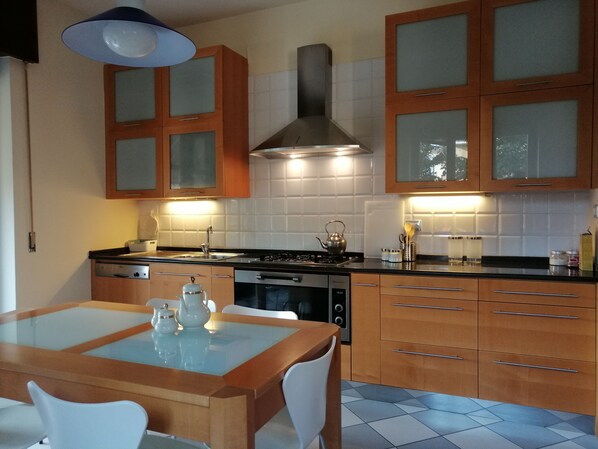 A modern kitchen with wooden cabinets, a gas stove, a built-in oven, and a glass-top dining table with chairs. - VASARI APARTMENT VERONA 2 ROOMS NEAR STATION, STADIUM, CENTER (Verona)