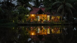 Una casa de techo rojo rodeada de agua y palmeras, con su estructura y luces reflejándose.