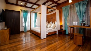 A four-poster bed with a canopy, wooden flooring, a wooden desk with a kettle, and a television on a stand.