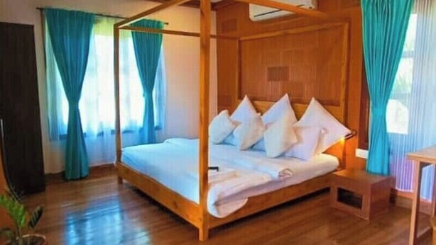 Una cama con dosel cubierta con sábanas y almohadas blancas, suelo de madera y una mesita de noche pequeña.
