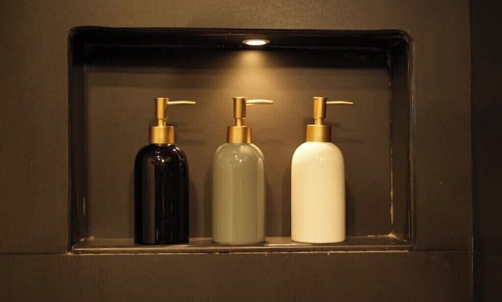 A shelf with three bottles of liquid soap in different colors.