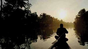 A silhouette of a person paddling a boat in a calm river surrounded by trees.