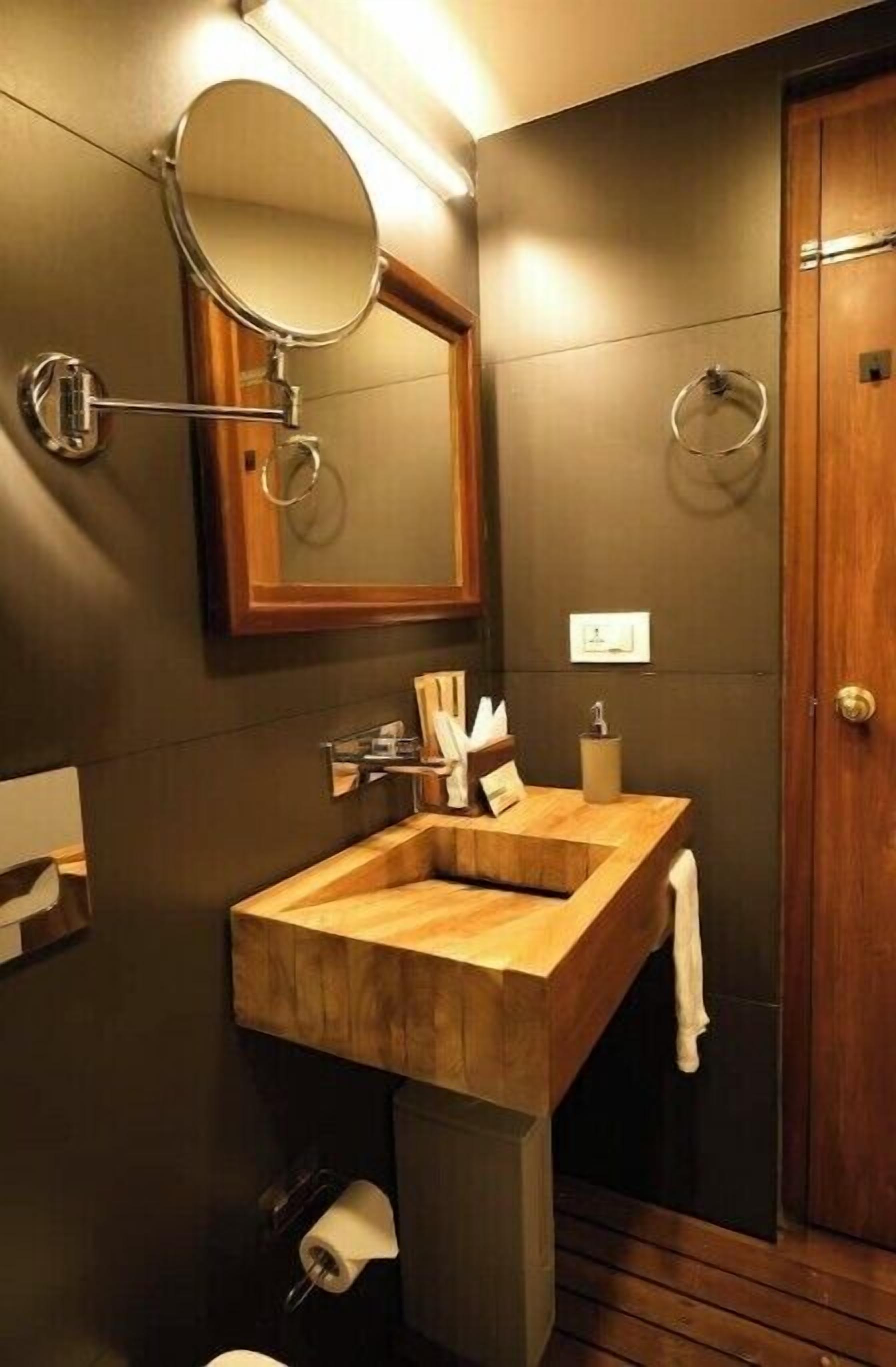 Une salle de bain moderne avec un meuble-lavabo en bois, un miroir rond et une porte en bois.