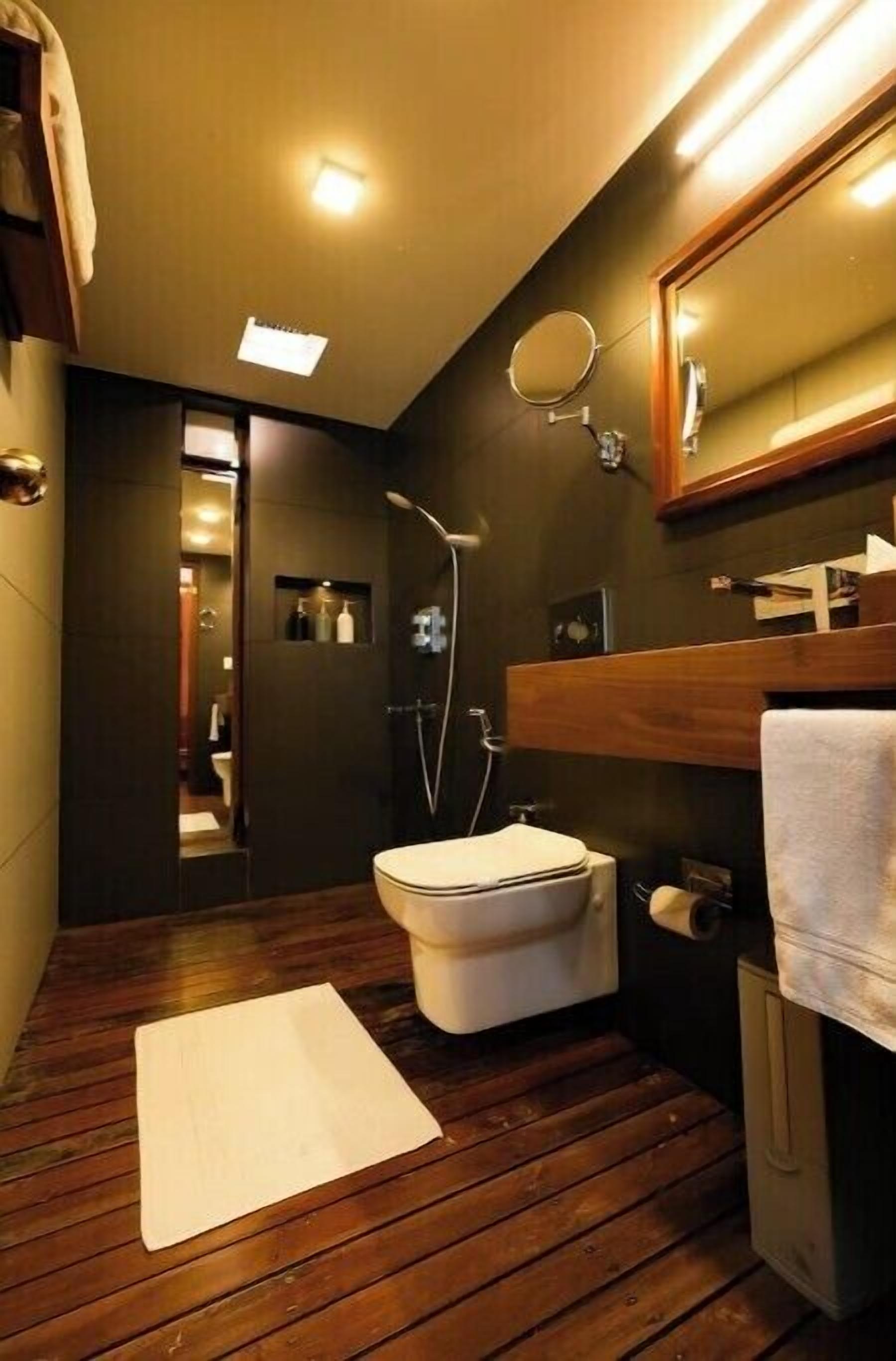 Une salle de bain moderne avec un plancher en bois, des toilettes blanches, une douche et un miroir au-dessus du lavabo.