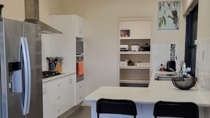 Une cuisine moderne dotée d’un réfrigérateur en acier inoxydable, de meubles blancs et d’un îlot central avec deux tabourets de bar noirs.
