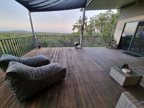 Eine Holzterrasse mit Landschaftsblick, ein überdachter Sitzbereich mit Kissen und ein kleiner Tisch mit Dekoration.