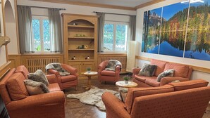 Un salon chaleureux, doté de meubles en bois, d’une cheminée et d’un grand tableau représentant un paysage de montagne.