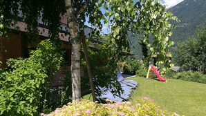 Un jardin bien entretenu, avec une pelouse verdoyante, une variété de plantes à fleurs et un espace de jeux pour enfants équipé d’un toboggan.