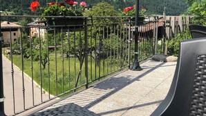 Un balcon avec une balustrade en métal, un lampadaire et une vue sur un paysage montagneux, avec des fleurs rouges au premier plan.