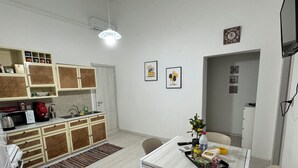 Une cuisine moderne avec des meubles blancs, une table à manger et des chaises. On y trouve un évier, un four à micro-ondes et une bouilloire. La pièce est éclairée par un luminaire et les murs sont décorés d’œuvres d’art.