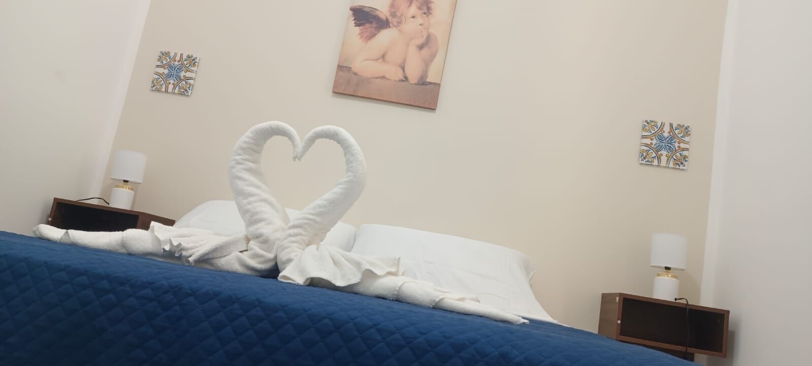Une chambre d’hôtel avec un lit, des oreillers, une décoration en forme de cœur faite avec des serviettes, un tableau au mur et des éléments décoratifs sur les murs.