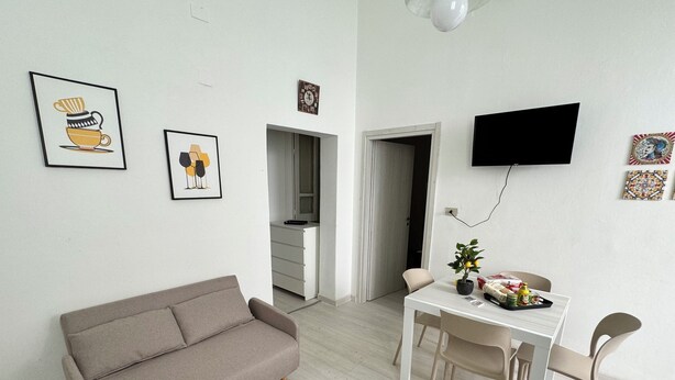 Un salon moderne comprenant un canapé, une table à manger, des chaises, un téléviseur et des œuvres d’art accrochées aux murs.