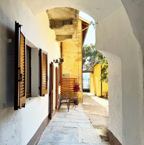 A narrow stone-paved alleyway with wooden shutters and a bench, leading to a yellow building with a gate. - Breeze - Vista Lago collection (Domaso)