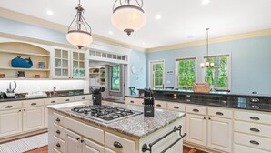 A spacious kitchen with a central island, white cabinetry, and a large window providing natural light. - Seaclusion at the Beach (Pawleys Island)